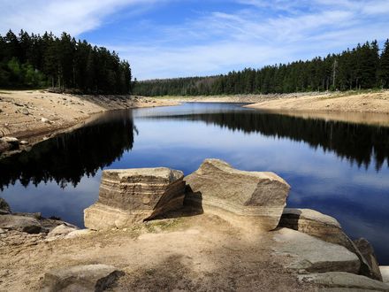 Zusehen ist der Oderteich in Sankt Andreasberg. Im vorderem Bild sind zwei große Steine und um dem Oderteich ist Fels und Wald.